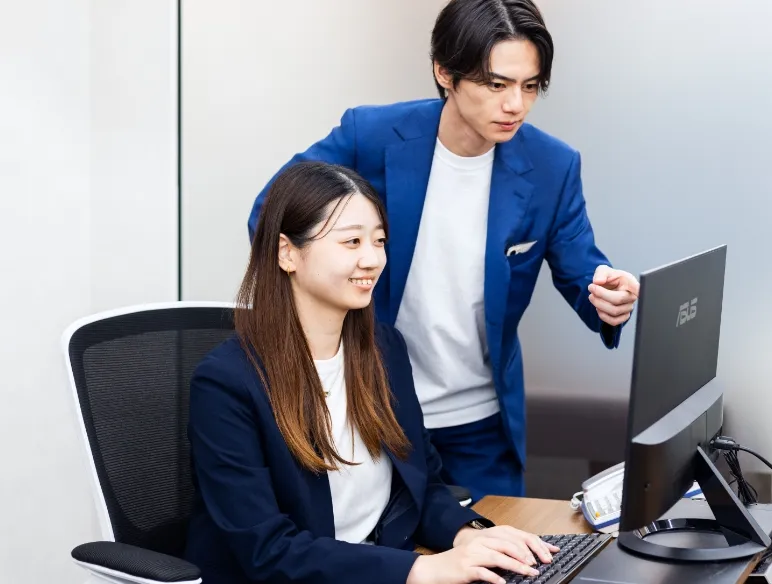 女性スタッフがパソコンのキーボードを打ちながら、男性スタップが画面を見ながら談笑している様子