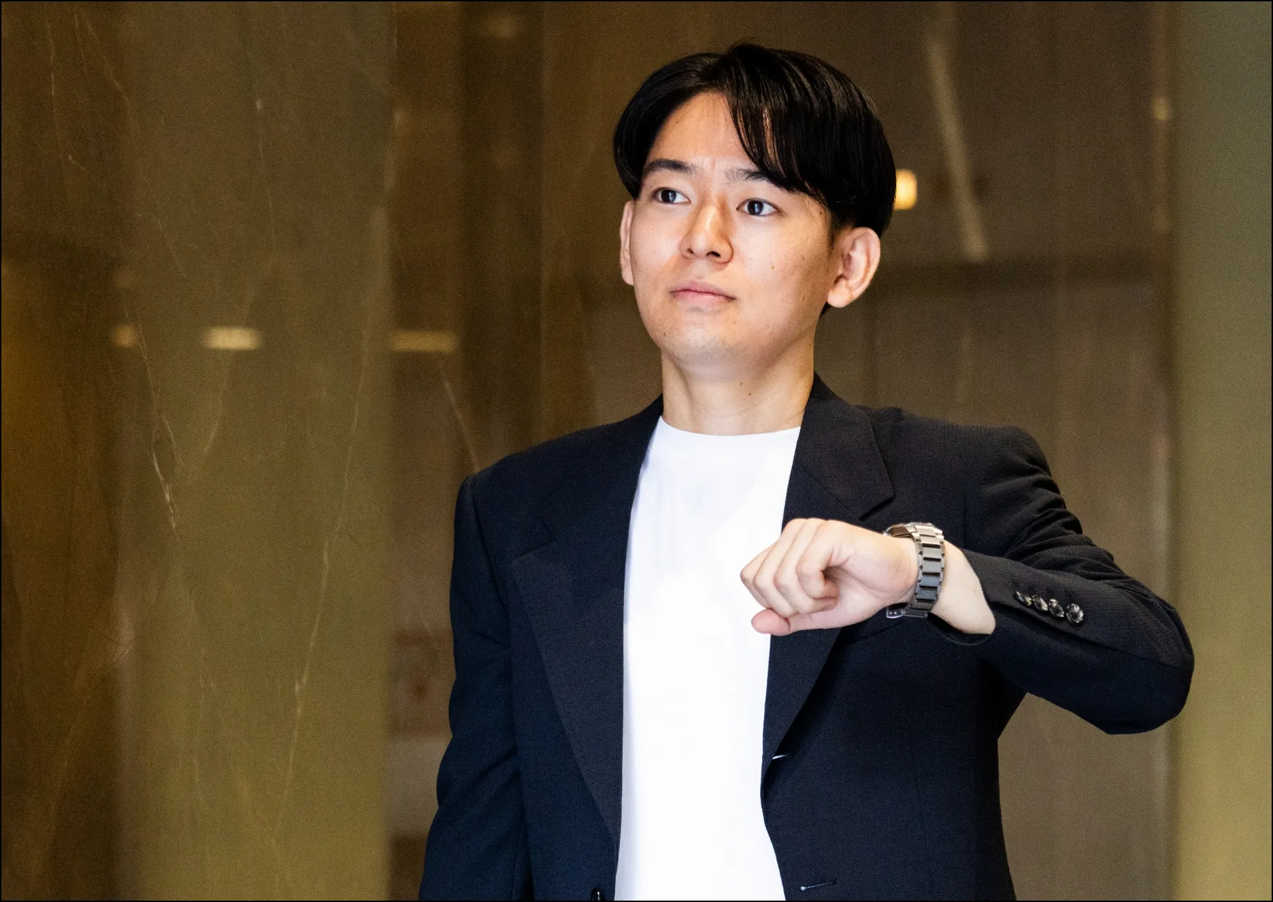 スーツ姿で腕時計を確認しながら、真剣な表情で先を見据える男性社員